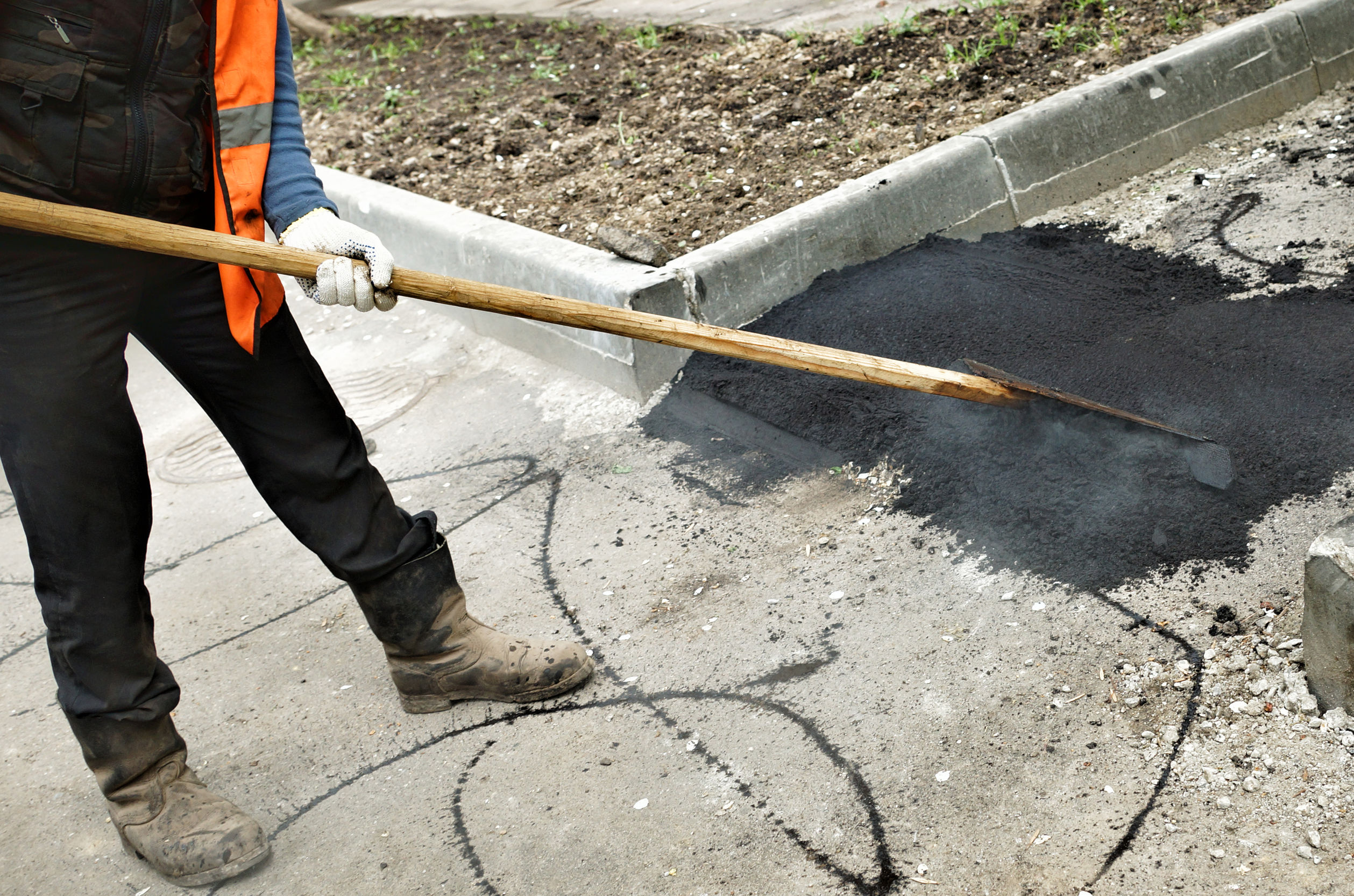 Worker using tool to level hot and steamy black asphalt
